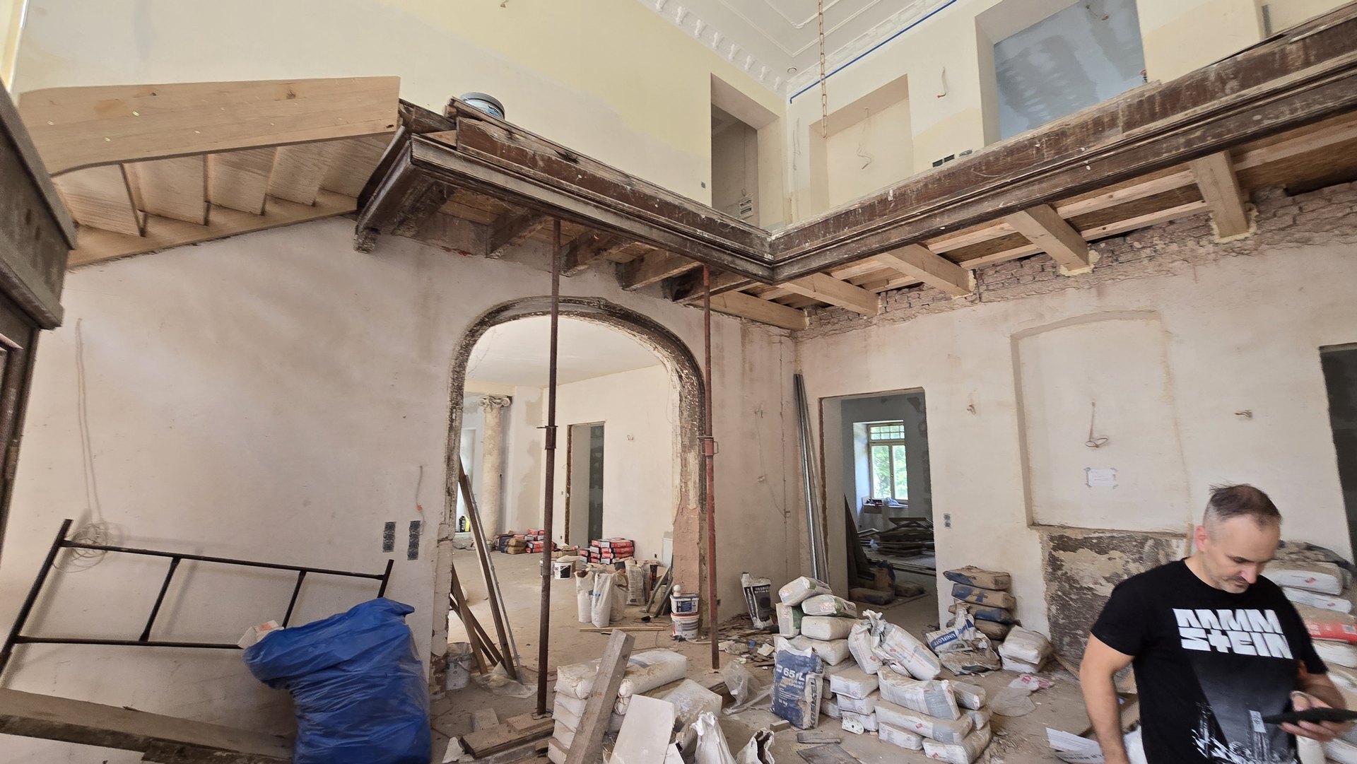 Widok od dołu na drewnianą konstrukcję galerii i duże łukowe przejście w remontowanym holu